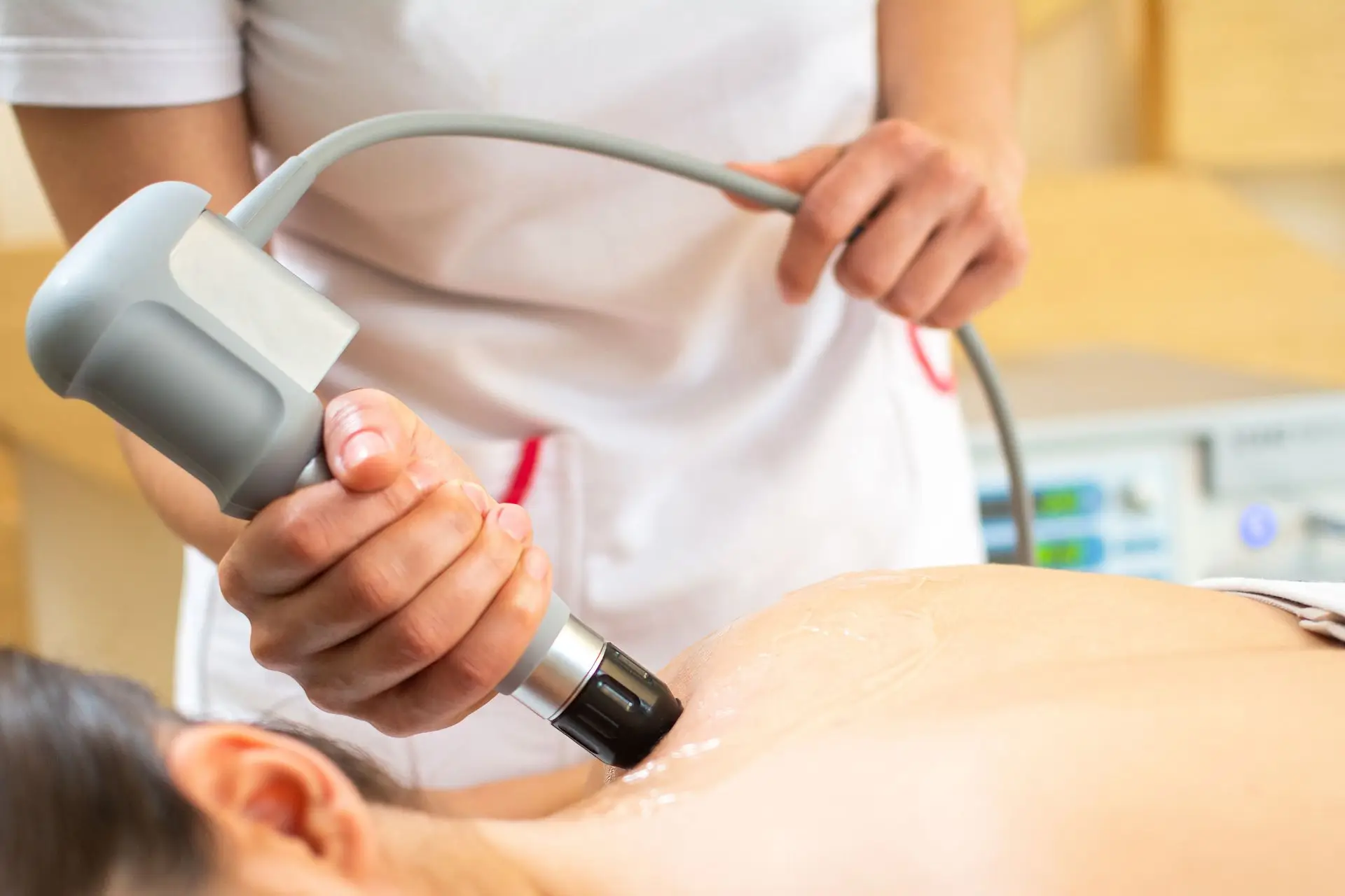 Frau liegt am Bauch mit freiem Rücken auf dem jemand mit der Hand eine Ultraschalltherapie-Sonde führt
